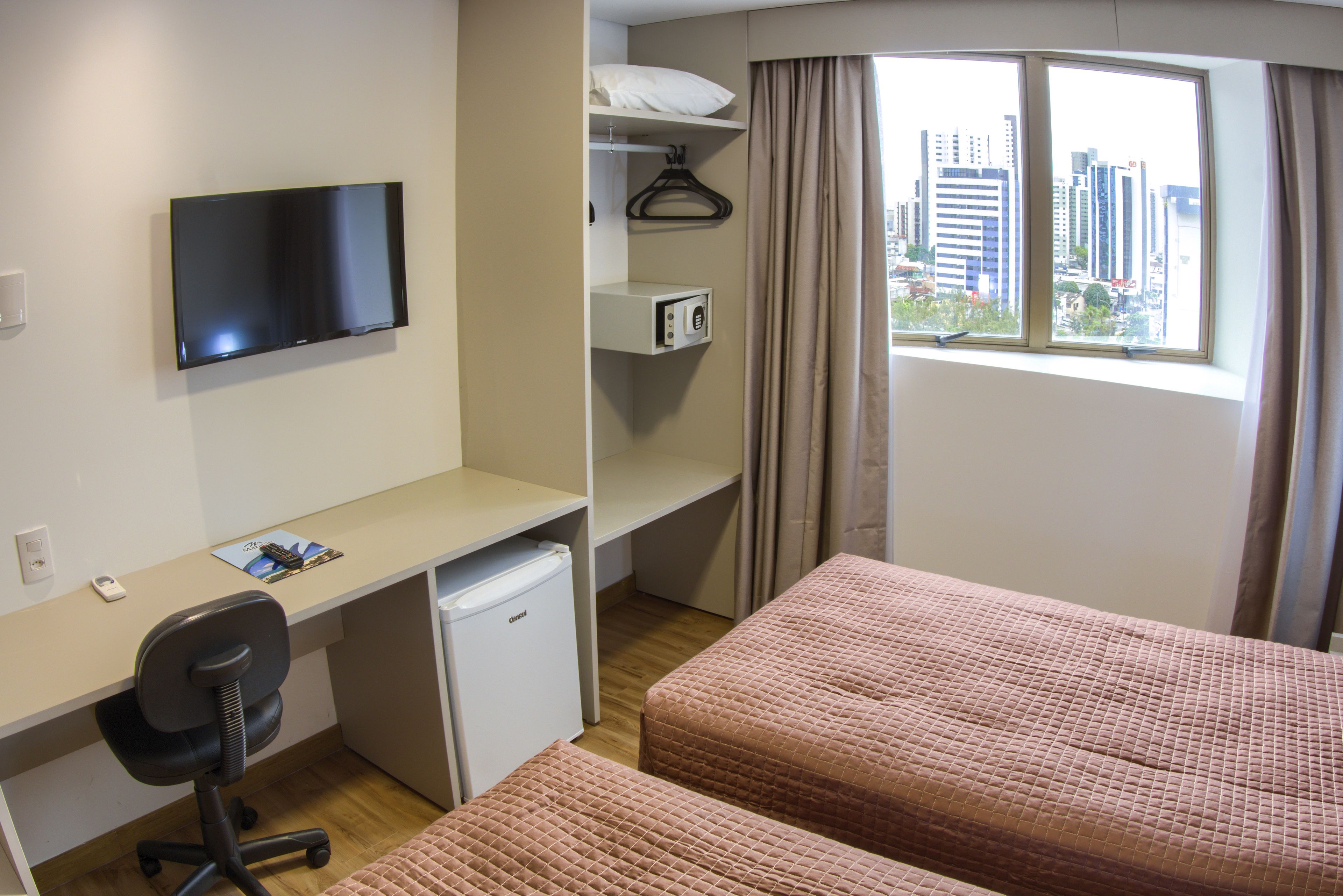 A hotel room with a desk, a television, a mini-fridge, a microwave, a bed, and a window with a city view.