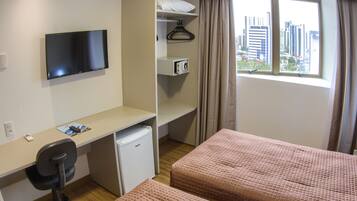 A hotel room with a desk, a television, a mini-fridge, a microwave, a bed, and a window with a city view.
