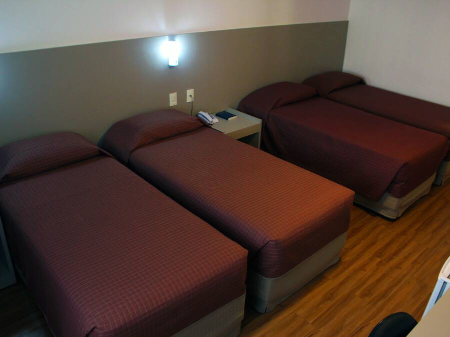Una habitación con tres camas individuales, una mesita de noche con teléfono y una lámpara fijada a la pared.