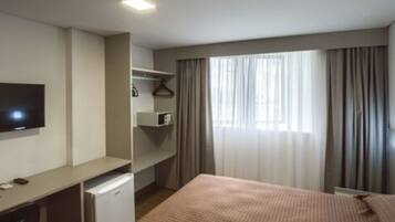 Una camera d'albergo con un letto, una scrivania, una televisione e una finestra con tende.