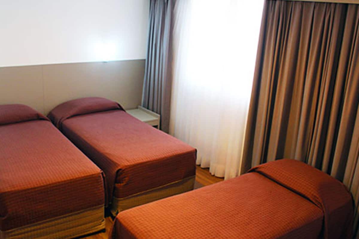 Une chambre avec trois lits simples, une petite table et une fenêtre avec des rideaux.