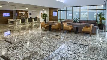 A hotel lobby with a reception desk, seating area, and large windows.