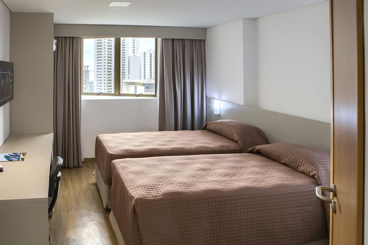 Une chambre d’hôtel avec deux lits, un bureau et une fenêtre avec des rideaux.