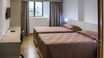 A hotel room with two beds, a desk, a chair, a TV, and a window with curtains.