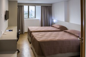 Quarto de hotel com duas camas, uma mesa, uma cadeira, uma televisão e uma janela com cortinas.