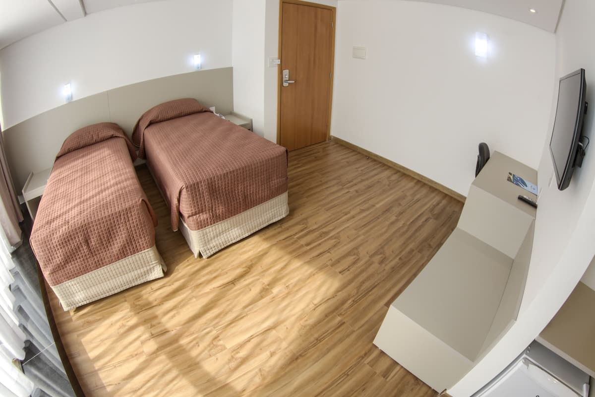 Une chambre avec deux lits, un plancher en bois, une porte, une télévision et une petite table.