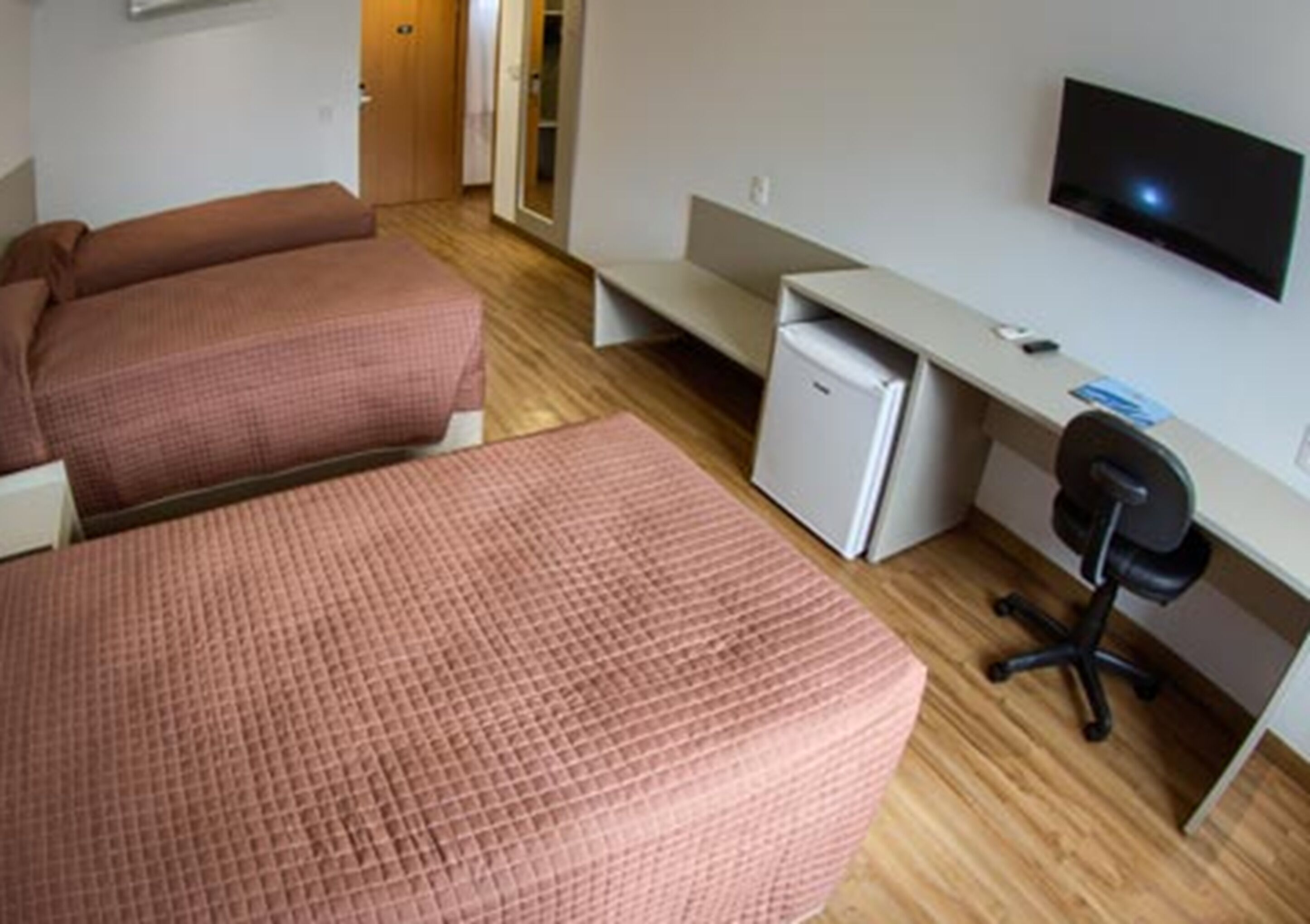A bedroom with two beds, a desk, a chair, a television, and a small refrigerator.