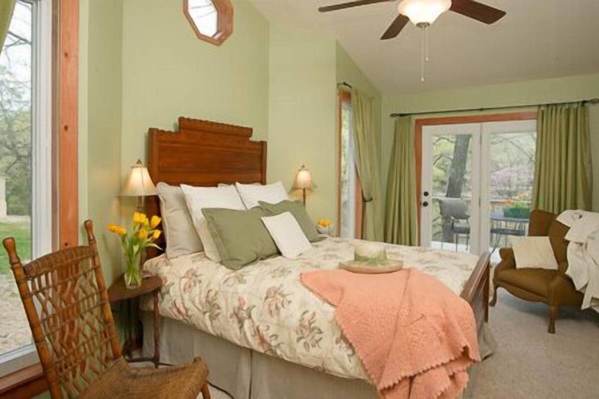 Quarto com cama, cadeira, mesa de cabeceira, abajur e janela com cortinas.