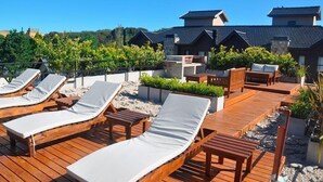 A wooden deck with lounge chairs and a small table, surrounded by greenery and a stone wall. - Solar Pampa Apart Hotel (Mar de Las Pampas)