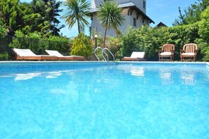 Ein klares, blaues Schwimmbecken mit Liegestühlen und einem Haus im Hintergrund.