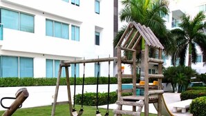 A playground with swings and a climbing structure in front of a white building with large windows. - Apartamentos Morros 427 Cartagena (Cartagena)