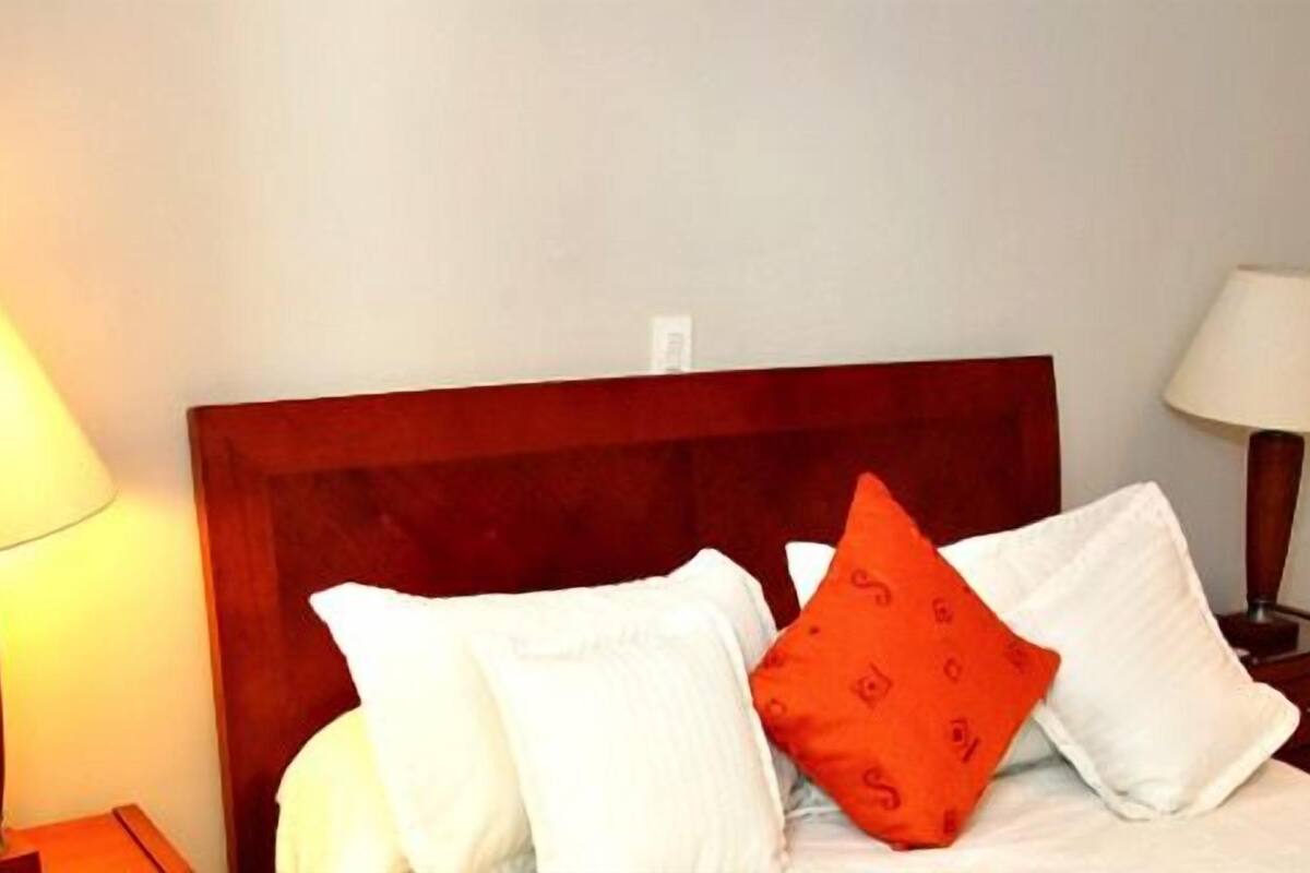 A hotel room with a wooden headboard, white bedding, and two bedside lamps.