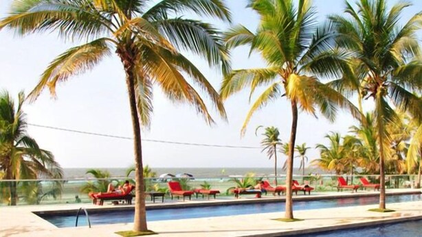 A poolside area with palm trees, red lounge chairs, and a view of the ocean. - Apartamentos Morros 427 Cartagena (Cartagena)