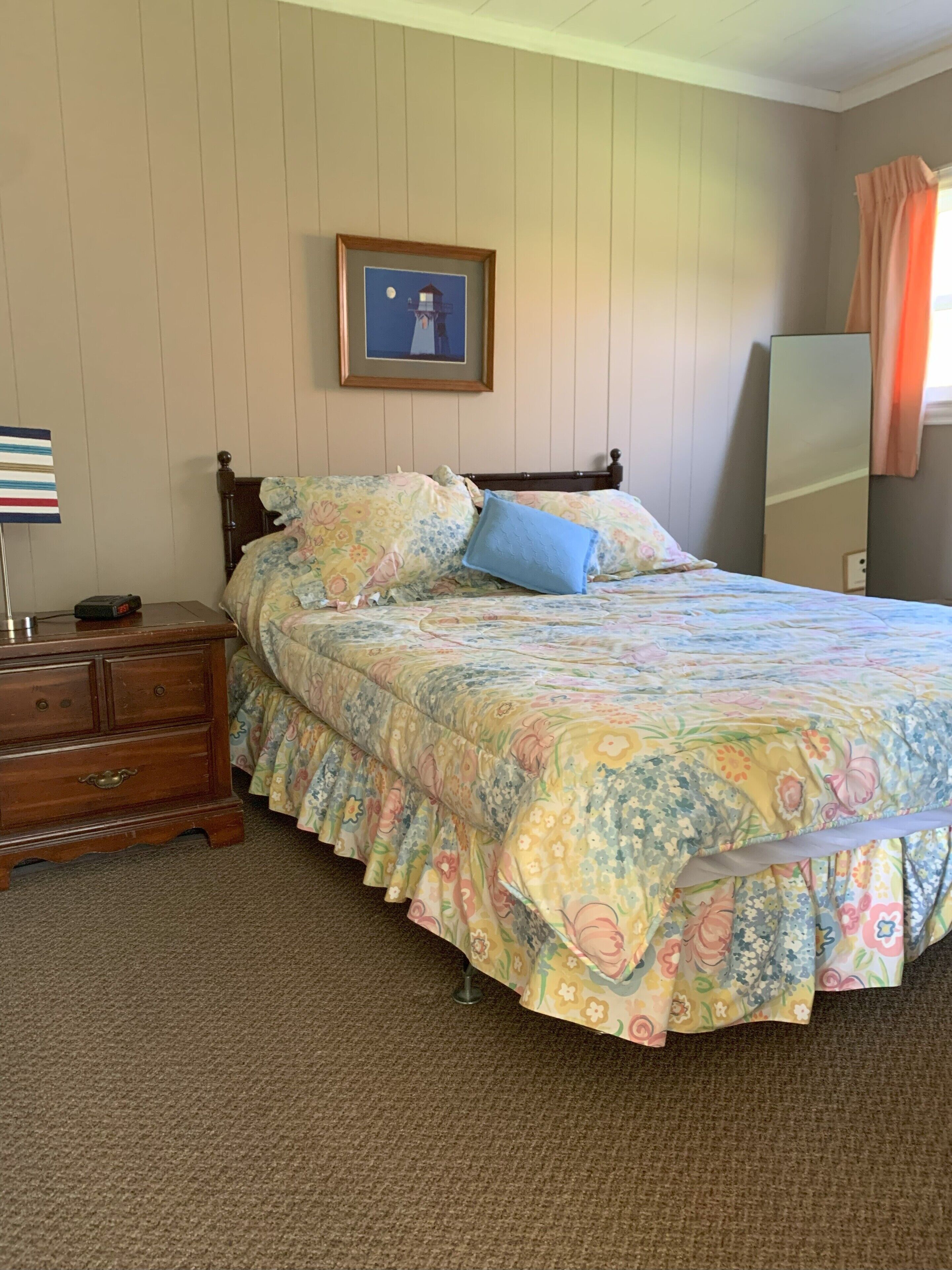 A bedroom with a bed, a dresser, a mirror, and a framed picture on the wall.