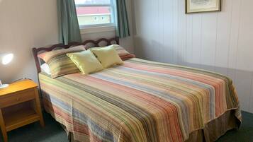 A neatly made bed with a striped bedspread, a wooden nightstand with a lamp, and a window with curtains.