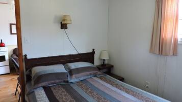 A bedroom with a wooden bed, two bedside tables, a wall-mounted lamp, and a window with curtains.