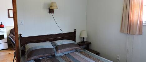 Un dormitorio con una cama de madera, dos mesitas de noche, una lámpara de pared y una ventana con cortinas.