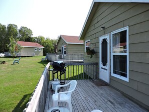 Eine Holzterrasse mit Gartenmöbeln, einem Grill und einem Haus mit weißer Tür und Fenster.