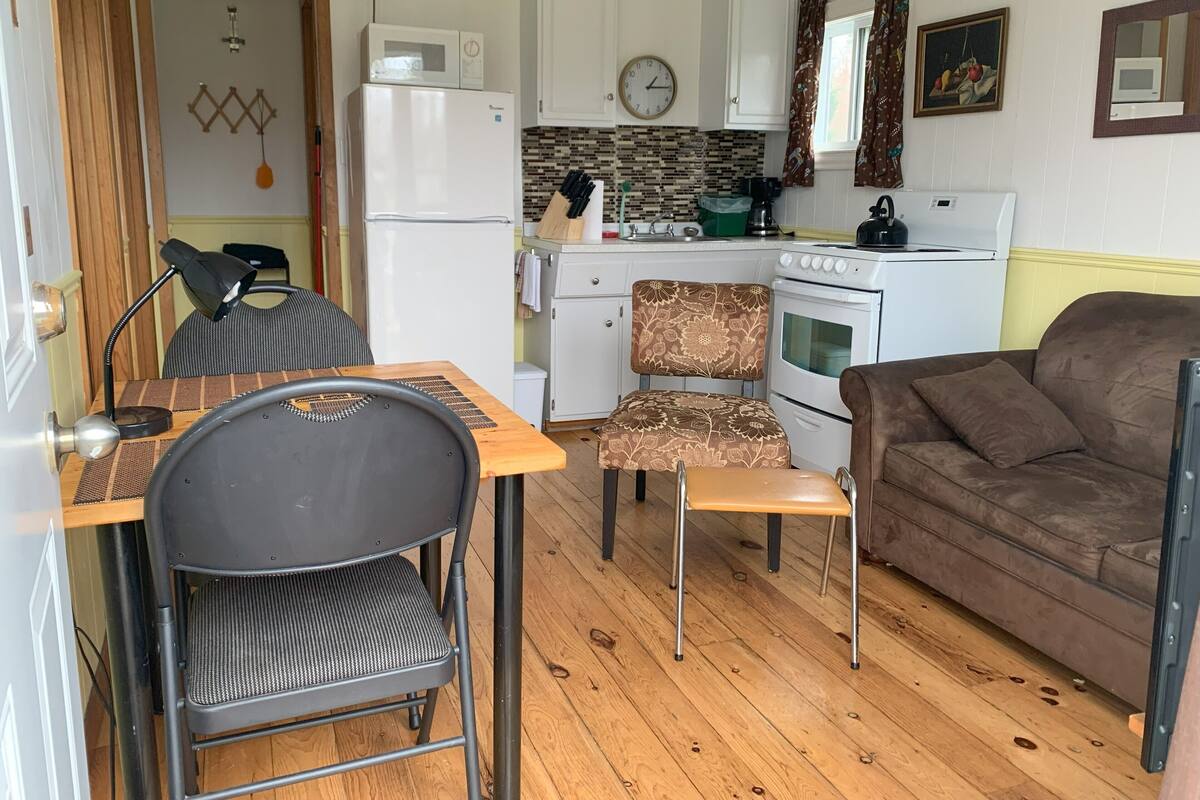 A compact kitchen with a refrigerator, microwave, stove, and sink. There is a dining area with a table, chairs, and a sofa.