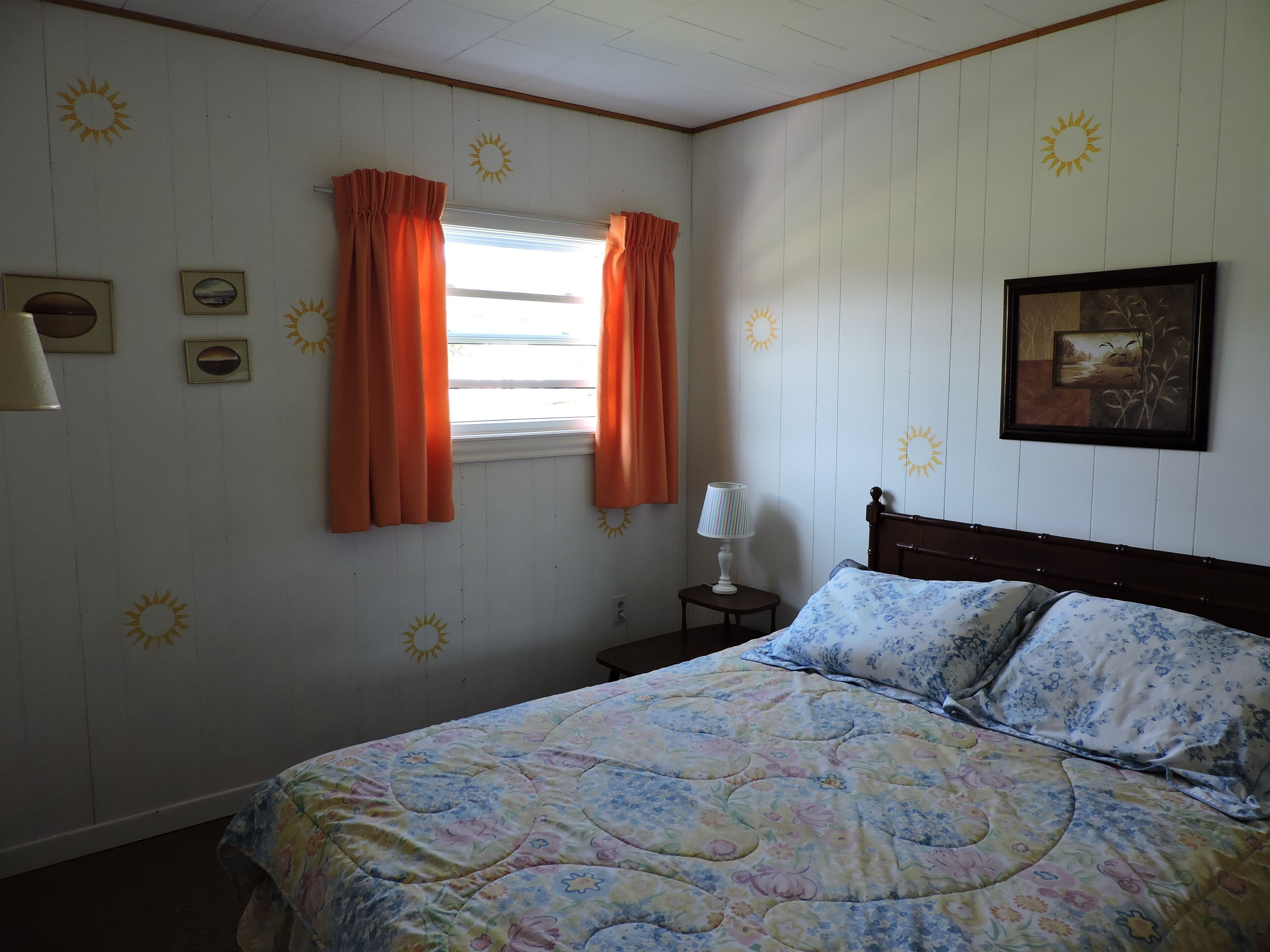 A bedroom with a bed, a nightstand, a lamp, a window with curtains, and wall decorations.