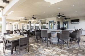 An outdoor patio area with wicker furniture, a stone-tiled floor, and ceiling fans.