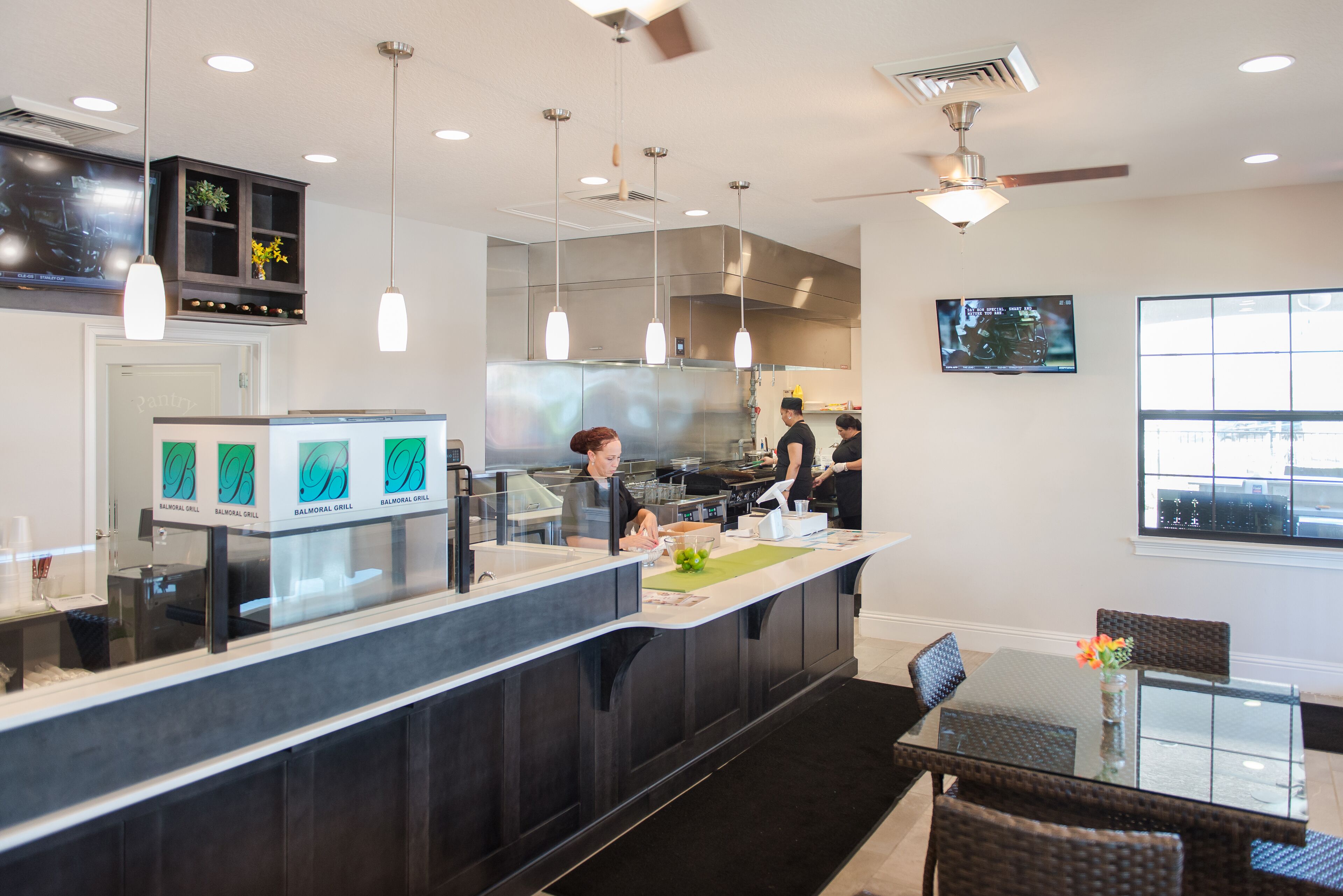 Una cocina moderna con una isla central, iluminación colgante y un comedor con mesa de vidrio y sillas de mimbre.
