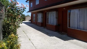 A two-story building with a red exterior, multiple windows, and a concrete pathway. - Cabañas ROHE (Puerto Montt)