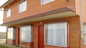 A two-story house with a red door and large windows with white curtains. - Cabañas ROHE (Puerto Montt)