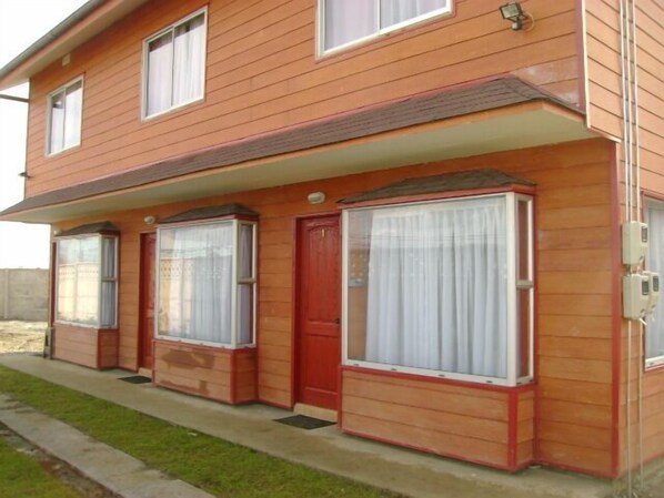 A two-story house with a red door and large windows with white curtains. - Cabañas ROHE (Puerto Montt)