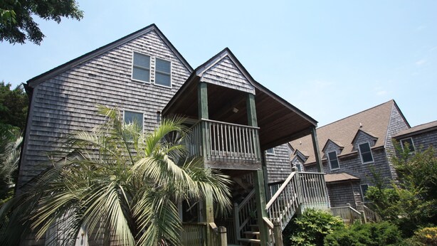 A two-story wooden house with a porch and a staircase leading to the second floor.
