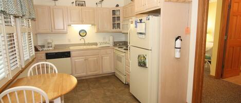 Una cocina compacta con muebles de madera, un refrigerador, un fregadero y una mesa de comedor con sillas.