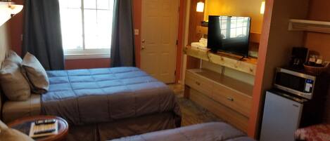 A hotel room with two beds, a ceiling fan, a television, a microwave, and a small table with books.