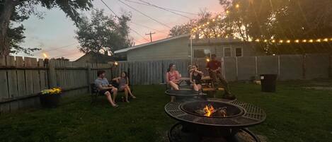 A backyard with a fire pit, a wooden fence, and string lights.
