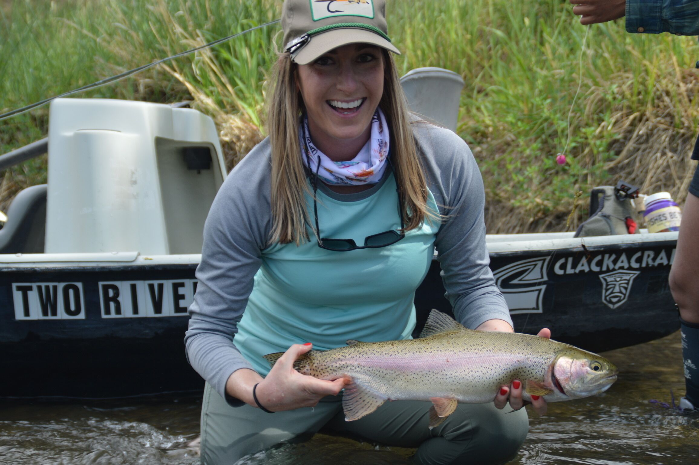 A person holding a fish near a boat with "TWO RIVER" written on it.