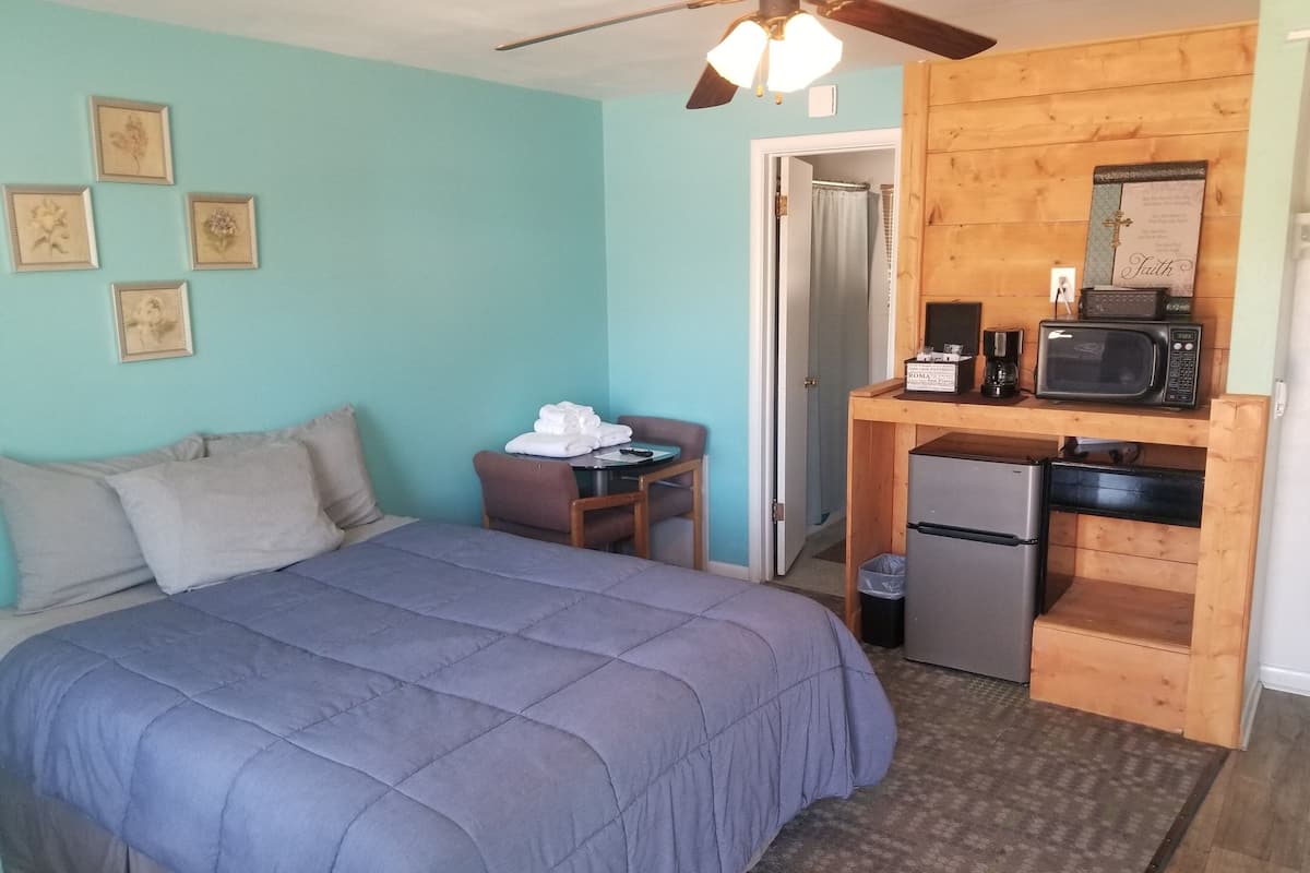 A bedroom with a bed, a small table with towels, a microwave, and a refrigerator.