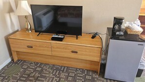 A television on a wooden dresser, a lamp, a coffee maker, and a refrigerator.
