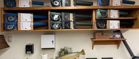 A room with shelves stocked with fishing tackle boxes, a fish decoration, a sink, and a telephone.
