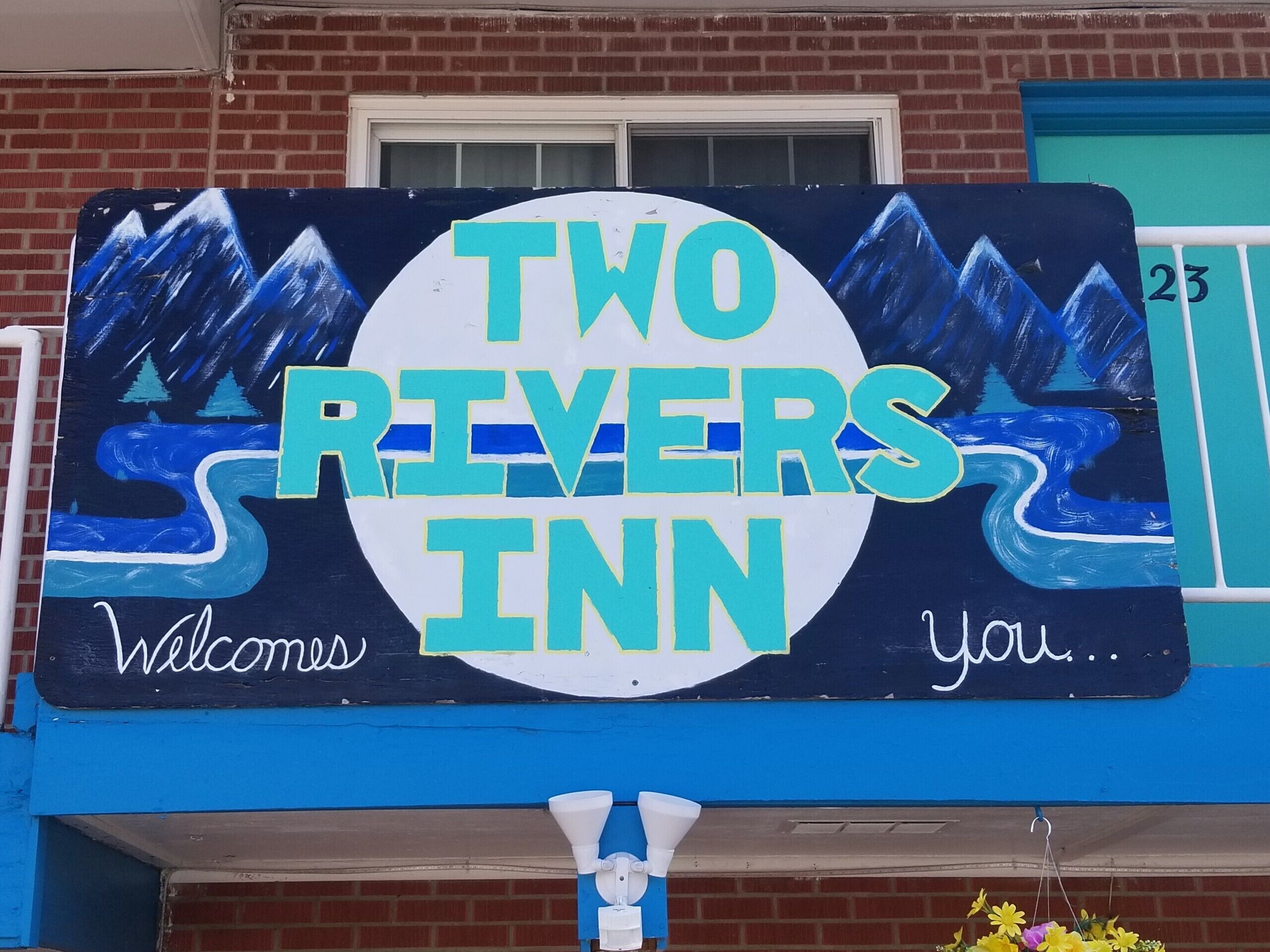 A sign for 'Two Rivers Inn' with a welcoming message and a decorative design.