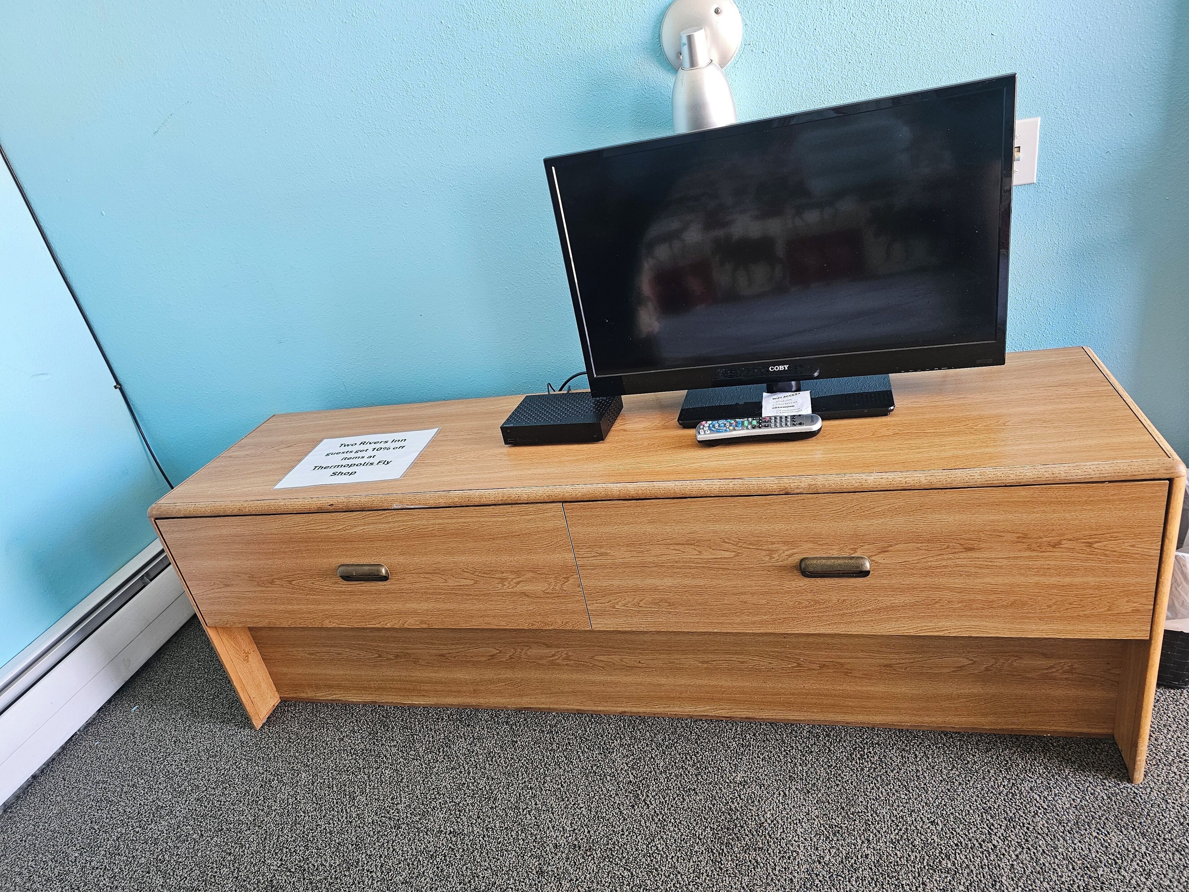 Ein Fernsehschrank aus Holz mit einem Flachbildfernseher, einer Fernbedienung und einem kleinen Schild.