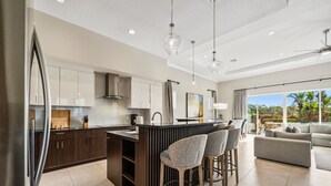 A modern kitchen with dark cabinetry, a central island, and bar stools. - Liberty Square: Private Pool, Games Room, Golf View, Near Disney (Kissimmee)