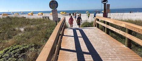 A wooden boardwalk leading to a beach with umbrellas and people walking.