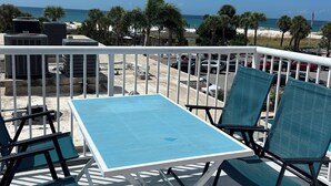 Un espace aménagé au bord de la piscine, avec une table et des chaises, donnant sur une plage bordée de palmiers et surplombant un ciel bleu azur.