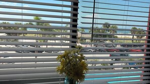 Une table sur laquelle est posé un vase de fleurs jaunes et un tapis bleu, le tout placé devant une fenêtre munie de stores horizontaux.