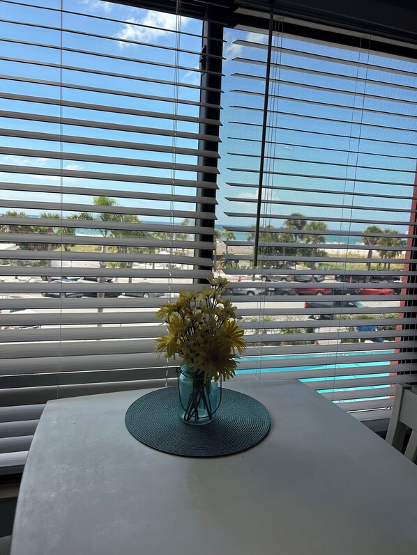 Een tafel met een vaas gele bloemen en een blauwe mat, voor een raam met horizontale zonwering.