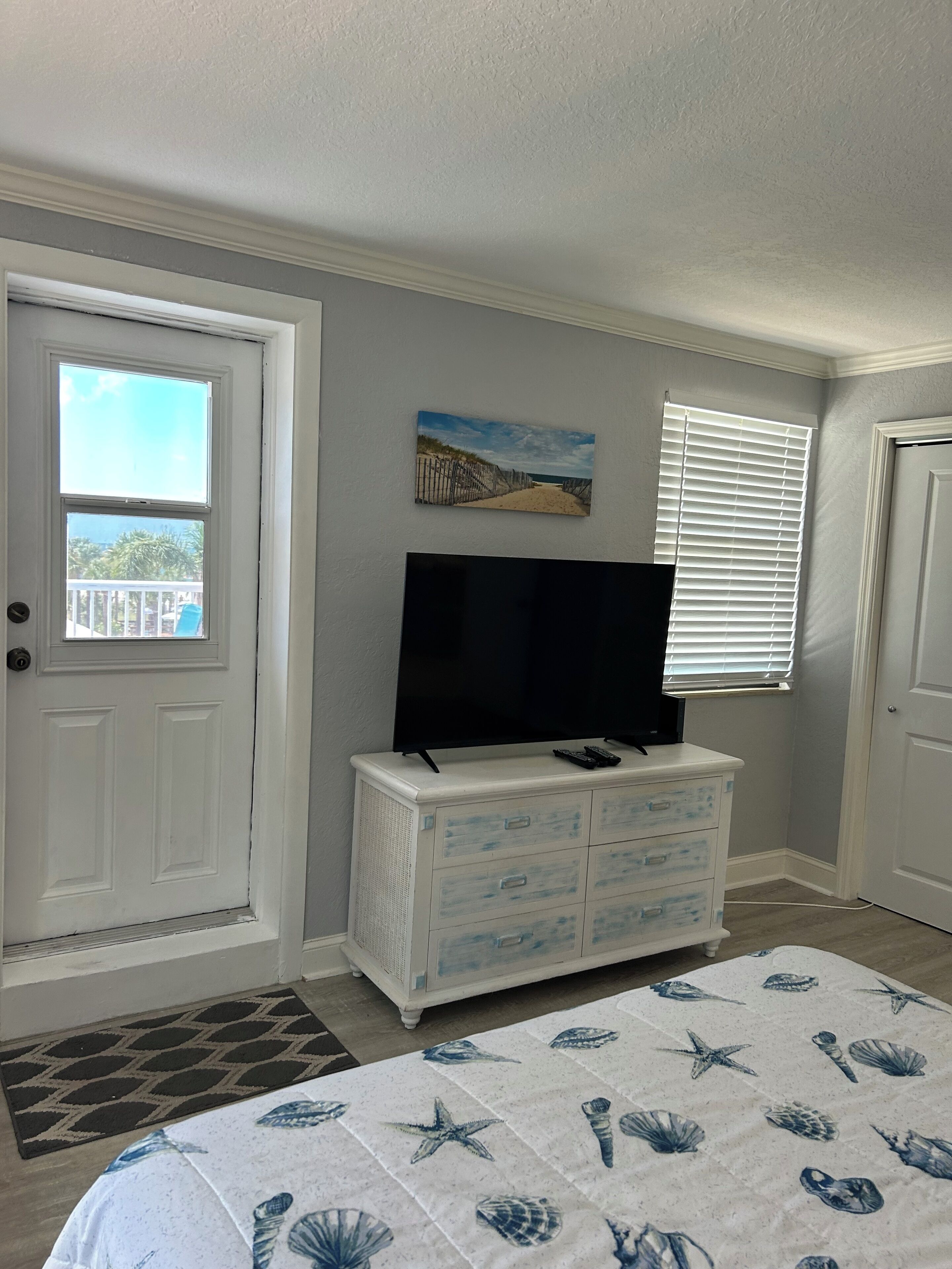 Une chambre à coucher avec un lit, une commode, un téléviseur et un tableau accroché au mur.