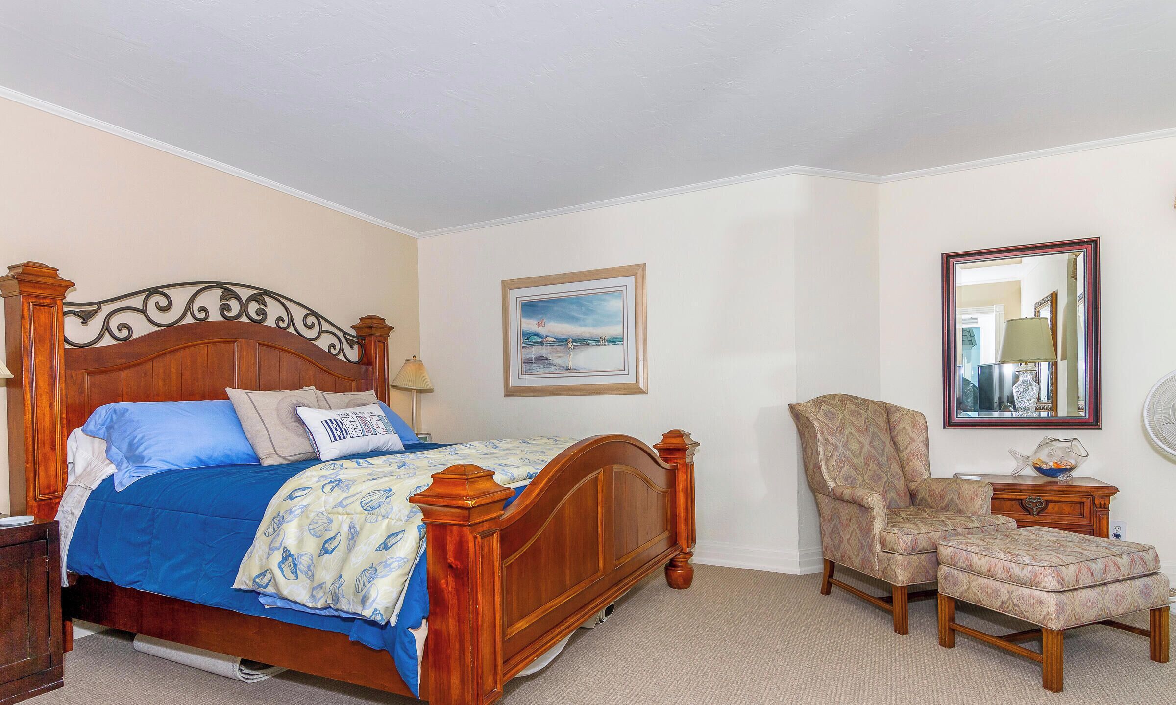 Une chambre à coucher avec un lit en bois, une chaise, un repose-pieds, une commode et un miroir.