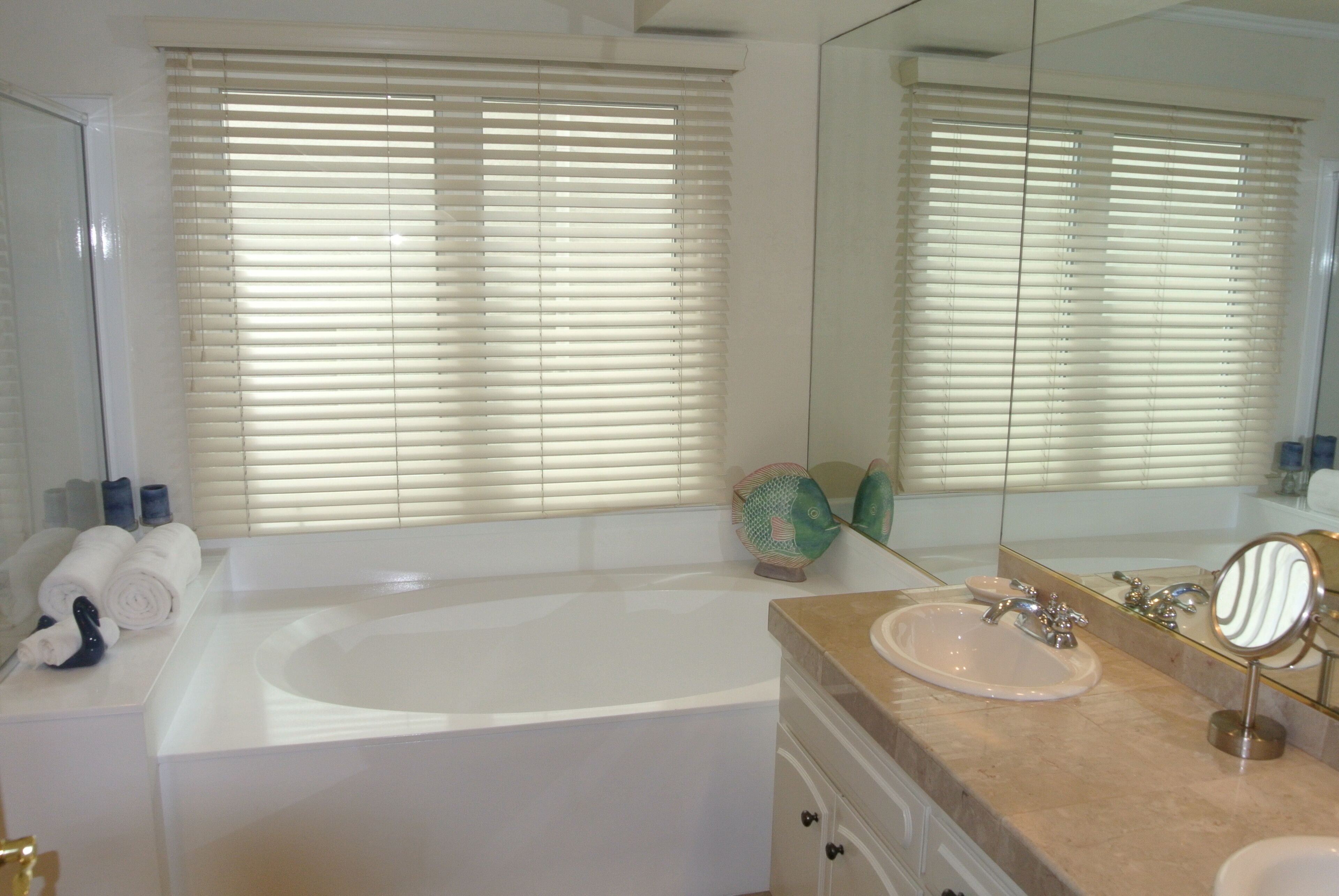 A bathroom with a bathtub, a sink, a mirror, and a window with blinds.