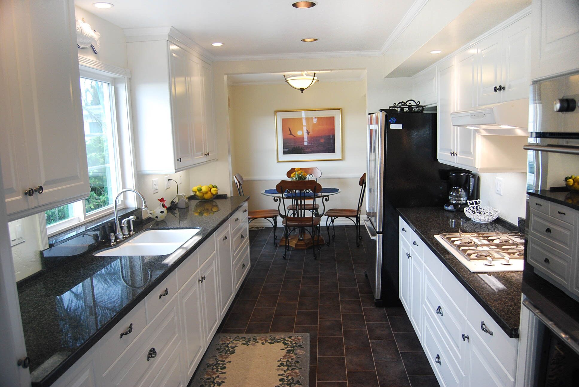 A kitchen with white cabinets, a black countertop, a dining area with a table and chairs, and a refrigerator.