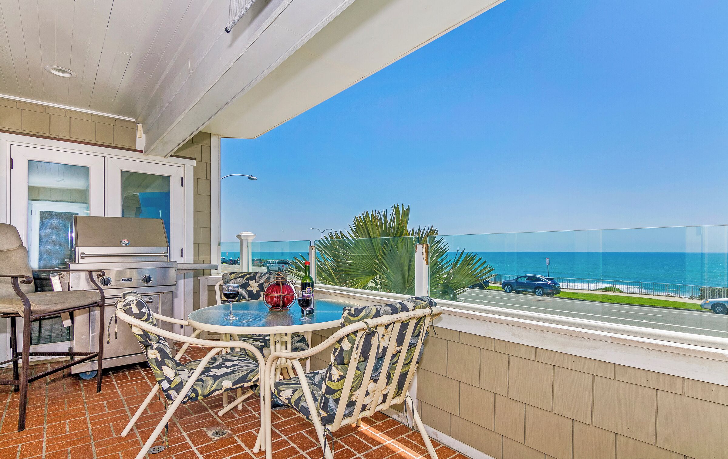 A balcony with a table and chairs, a grill, and a view of the ocean.