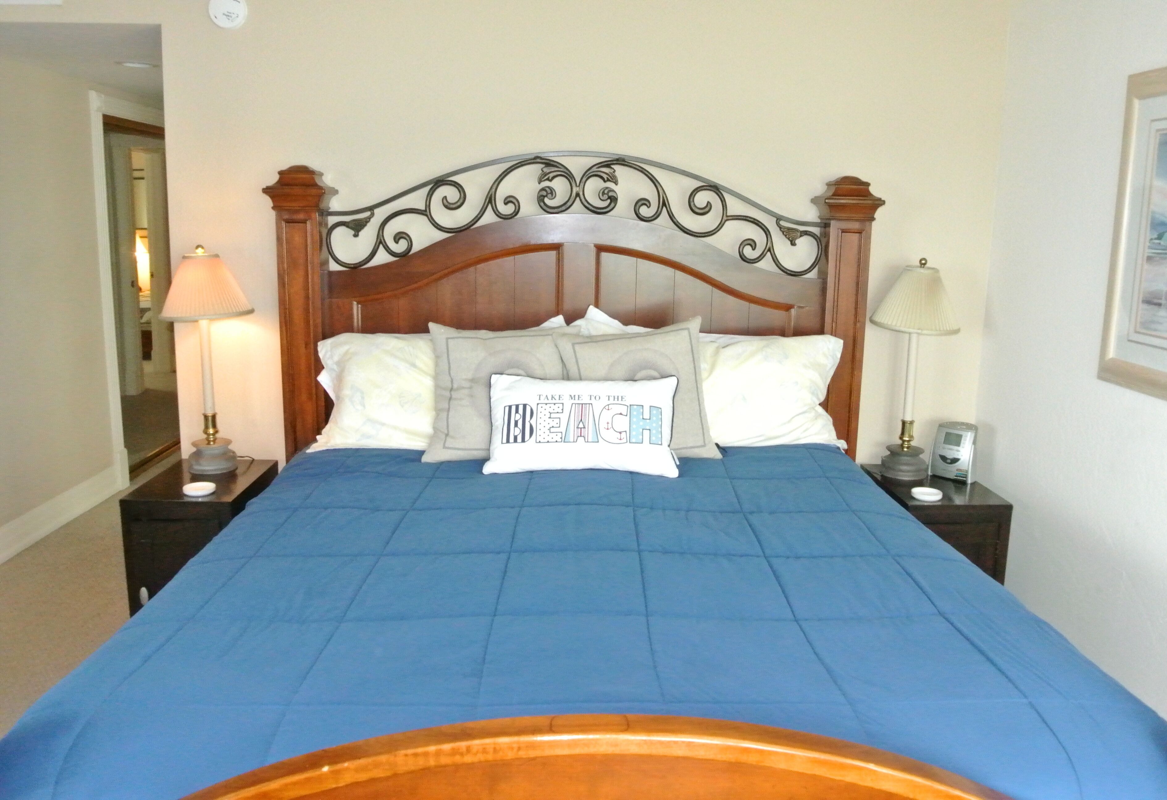 A neatly made bed with a blue bedspread, a decorative headboard, and two bedside lamps.
